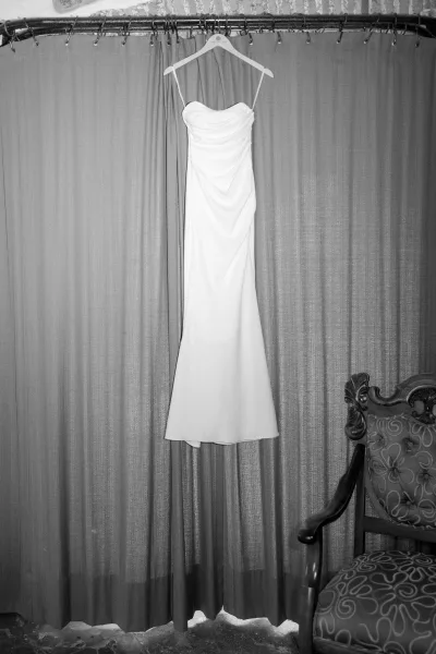 Wedding dress, strapless wedding dress hanging on a hanger from a curtain rod, draped bodice framed by curtains and a brick wall backdrop