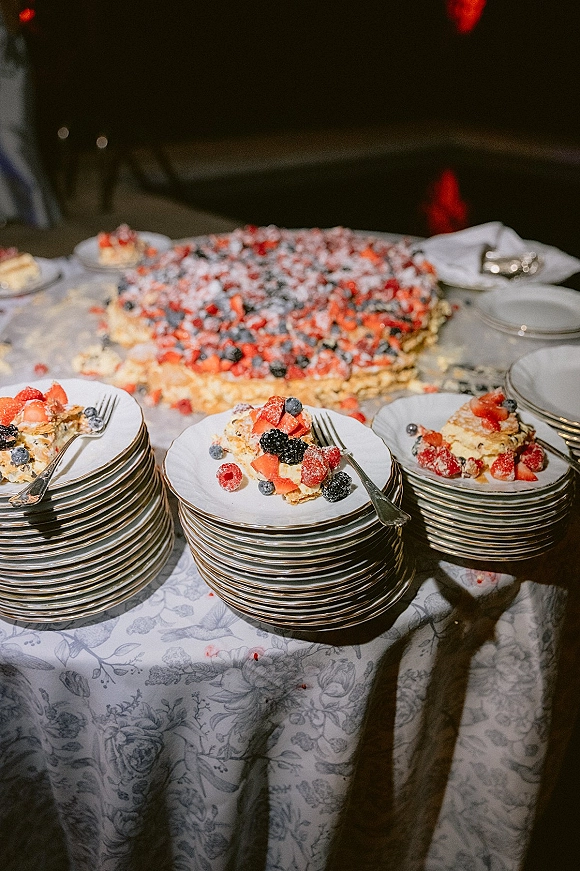 Wedding cake with berry wedding cake topping dusted in powdered sugar, sliced and served on plates at a dimly lit reception table