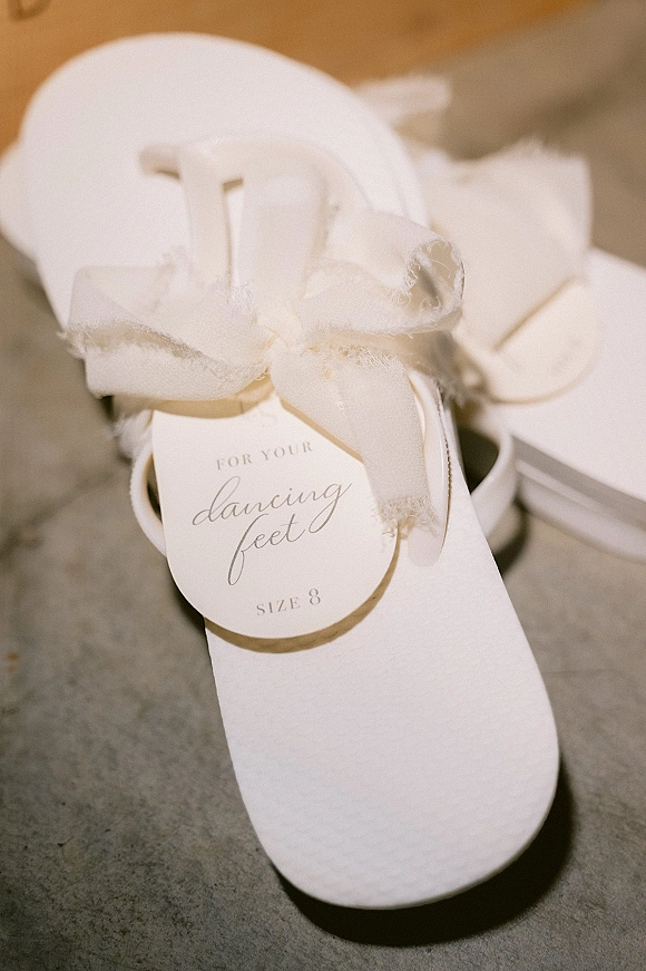 Wedding guest favors with reception flip flops tied in fabric bows and favor tags, neatly stacked on a stone floor