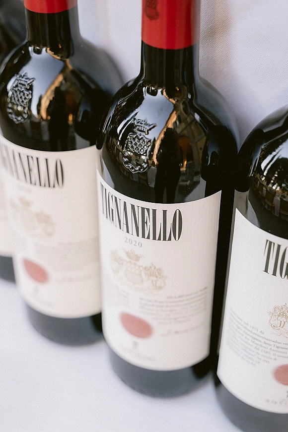 Wine bottles in a wedding bar setup lined up on a white tablecloth, showing bottle labels and red foil tops for reception service