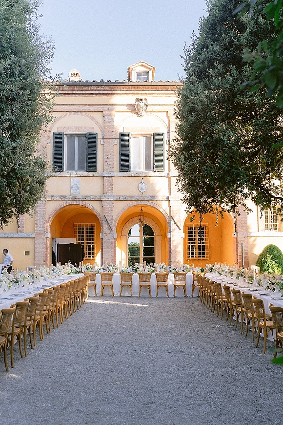 Reception tablescape with a long banquet table wedding setup, white linens and taper candles in a villa courtyard with arched doorways