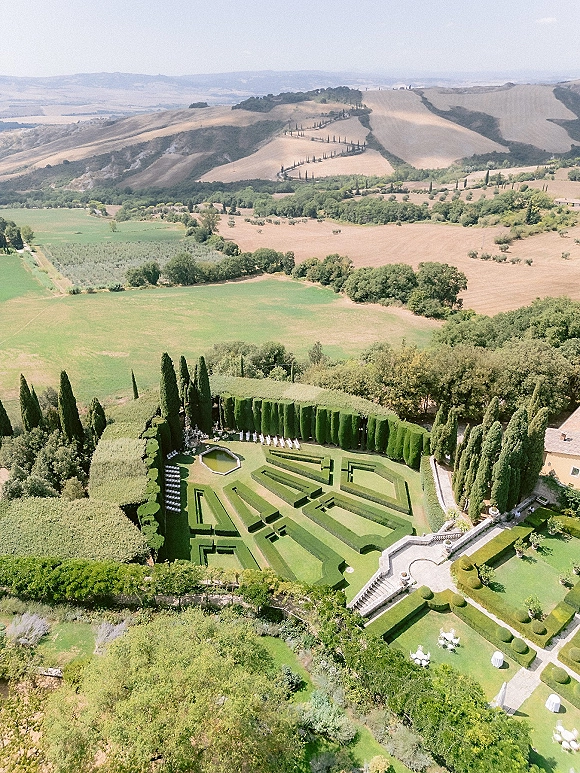 Garden wedding venue with hedge maze accent, white ceremony chairs on a stone terrace by a fountain overlooking rolling countryside hills