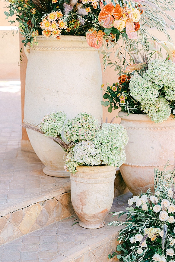 Wedding floral urns with lush hydrangeas, roses, and pampas grass on stone steps and terrace floor, framing the ceremony entrance