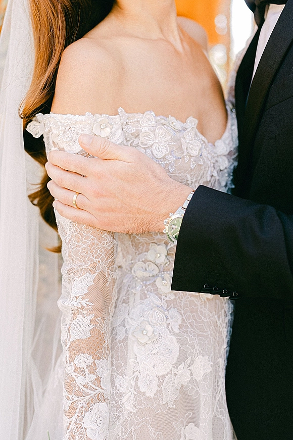 Wedding couple portrait with bride and groom close up, groom’s hand on her lace off-shoulder dress against warm orange wall bokeh lights