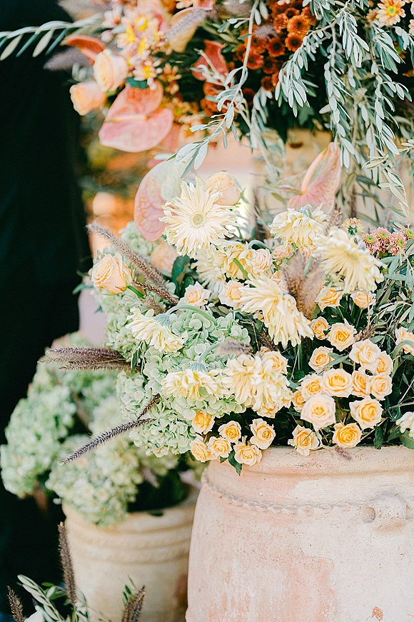 Wedding floral arrangement in a terracotta urn with peach roses, anthurium, mums, hydrangea, and pampas grass against a dark backdrop