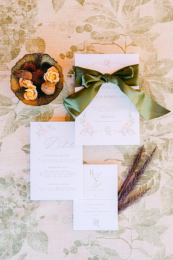 Invitation suite wedding invitation flat lay with green satin ribbon bow, RSVP and details cards, roses and walnuts on botanical linen backdrop