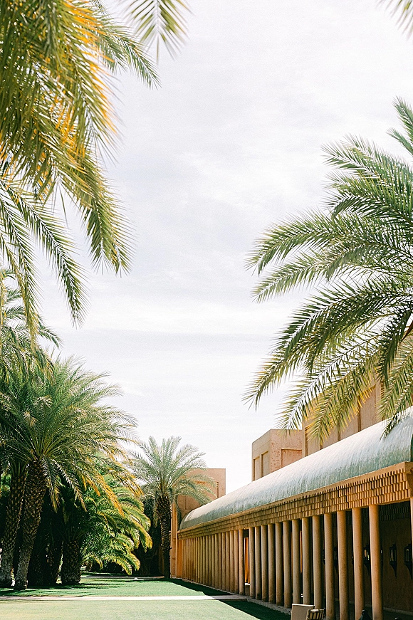 Wedding venue exterior with palm trees framing a green courtyard lawn and modern colonnade building under a clear sky