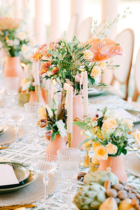 Reception tablescape with wedding table centerpiece, taper candles and peach vases, crystal stemware and fruit in soft window light