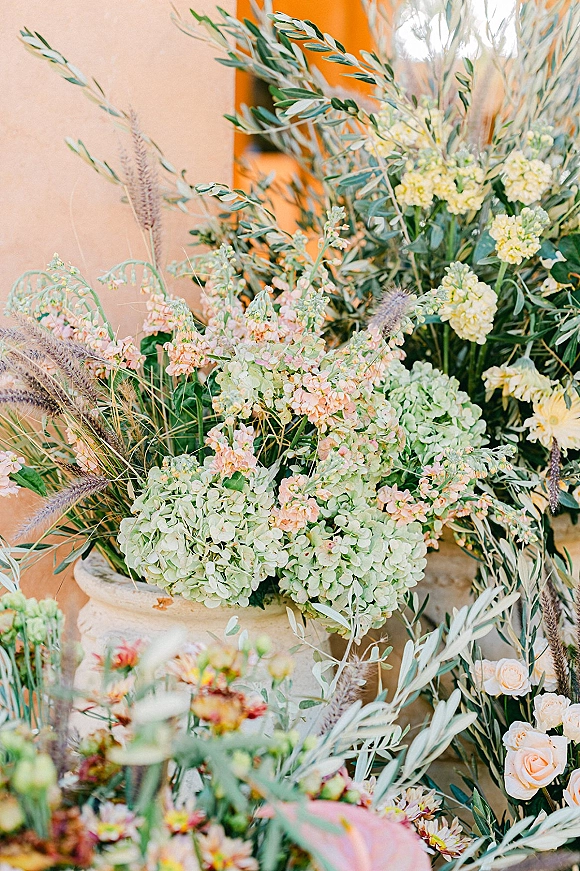Wedding floral arrangement overflowing from a stone urn with hydrangea and garden roses, set by a stucco wall and doorway
