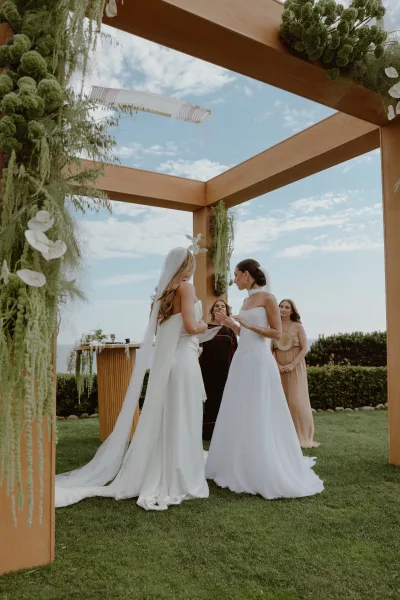 Ceremony moment as brides exchanging vows beneath a square ceremony arch, standing close as they face each other.