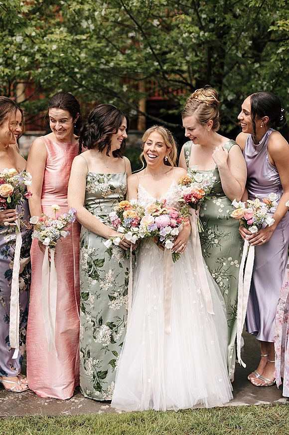 Bridesmaid group portrait with bride with bridesmaids holding colorful bouquets, one ribbon streamer, walking on stone path by green trees