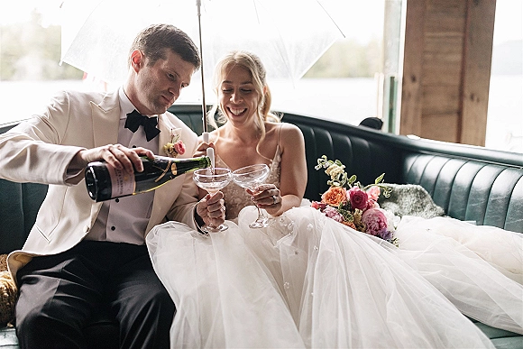 Wedding couple toast with a champagne toast wedding moment, sipping from coupe glasses inside a vintage car with open door and bouquet