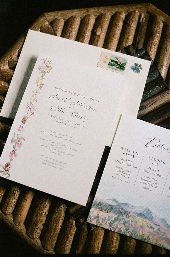 Wedding invitation suite with calligraphy wedding invitation and floral illustration, envelopes and postage stamps on woven rattan and dark fabric