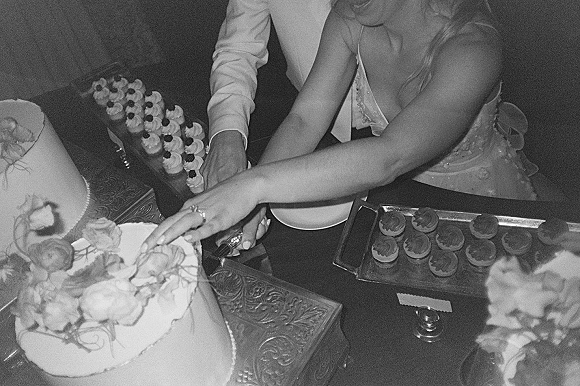 Cake cutting moment as bride and groom hold the knife over a floral-topped wedding cake beside a cupcake tower on the dessert table