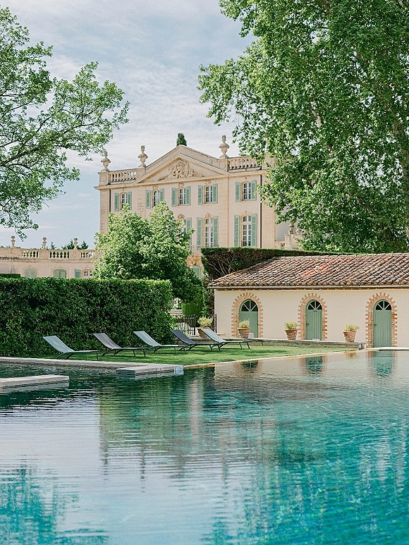 Wedding venue exterior of a historic villa with a swimming pool, lounge chairs, and potted plants amid garden hedges and trees