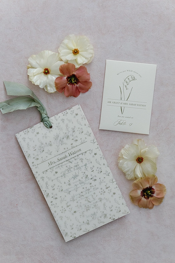 Wedding place card and wedding escort cards with floral print and ribbon, styled with flowers on a soft pink fabric backdrop