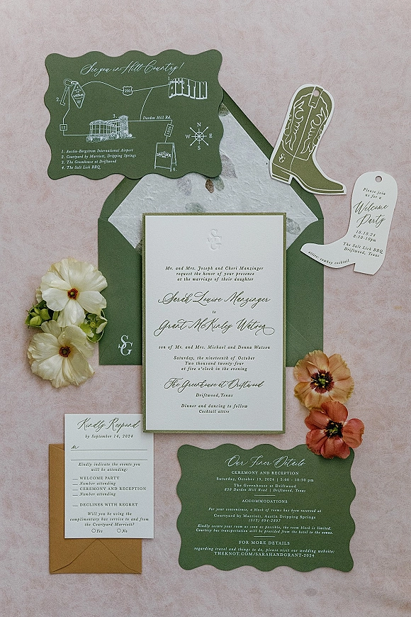 Invitation suite wedding invitation flatlay with deckle-edge cards, RSVP and map inserts, boot tag, monogram, floral sprigs on pink fabric backdrop