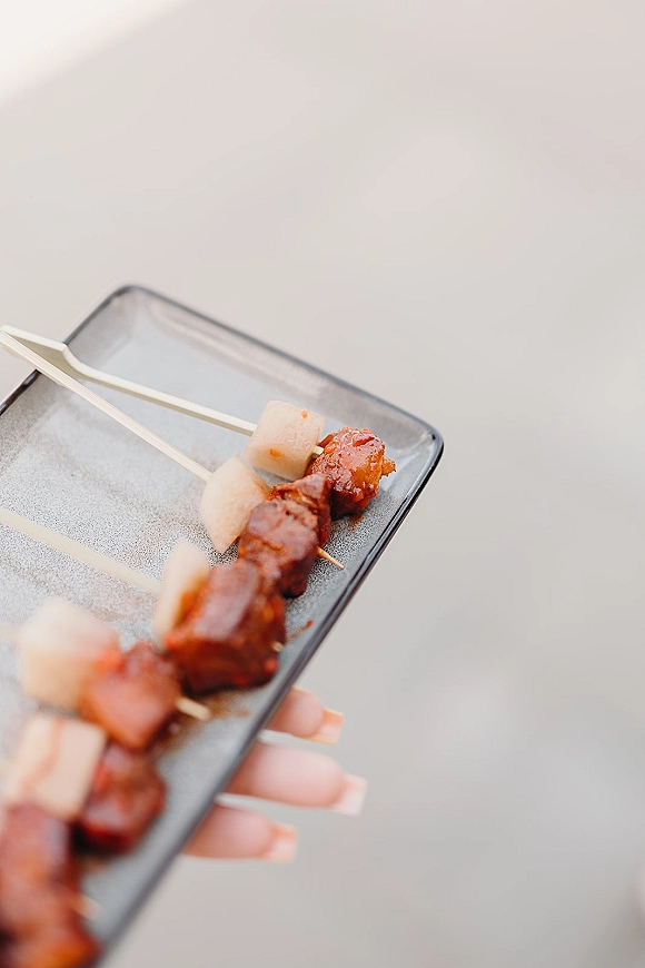 Wedding appetizers arranged on appetizer skewers on a serving tray, held by a hand against a neutral background for cocktail hour