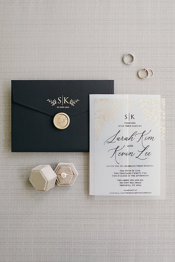 Wedding invitation suite with black and gold wedding invitations, wax seal, rings and ring box arranged on textured linen fabric