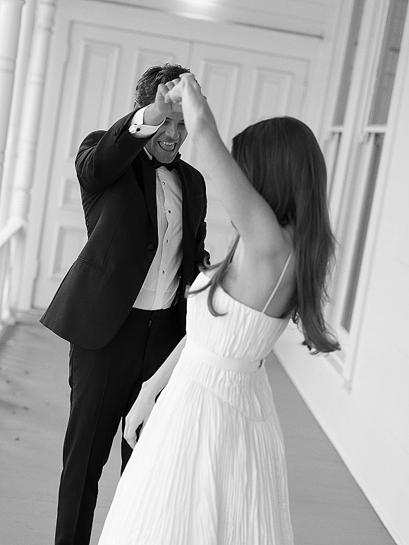 Couple dancing in a wedding twirl photo, bride spinning her dress as the groom in a tuxedo leads on a porch with white columns