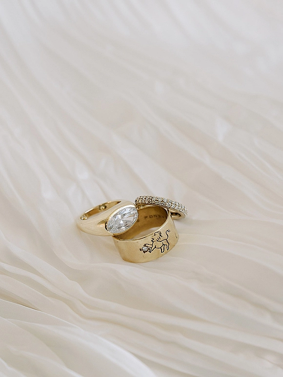 Wedding rings with a gold wedding band and oval diamond ring stacked on ivory tulle, with engraved details and a pavé band