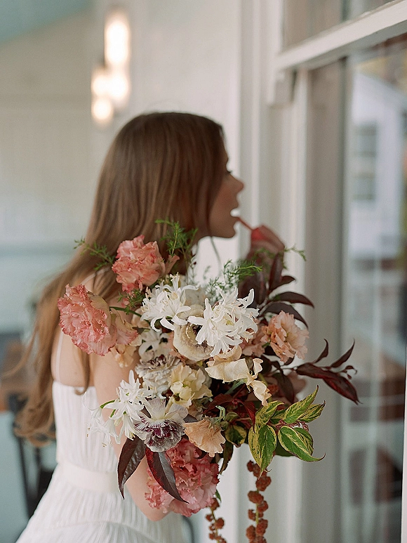 Bridal portrait of a bride holding bouquet in side profile, wearing a white strapless dress in an indoor hallway by a white door