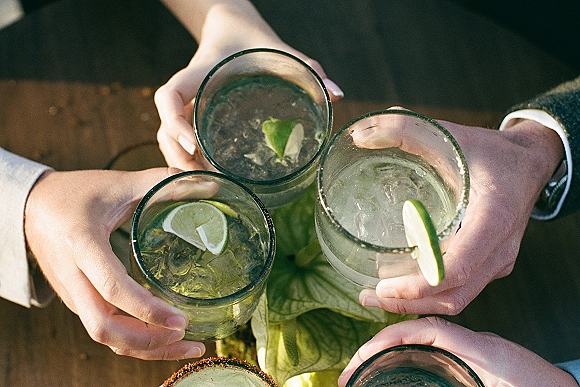 Wedding cocktail toast with bridesmaid drink toast as hands clink iced glasses with lime wedges and mint on a wooden table