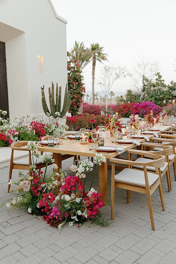Reception tablescape with an outdoor wedding reception table on a wood farm table, colorful bud vases and candles on a cactus-lined patio by water view