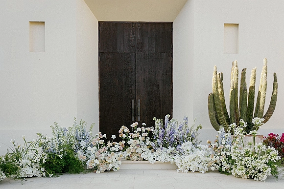 Wedding ceremony backdrop with ground floral ceremony flowers in blush, lavender, and white, set on stone steps before dark wooden doors