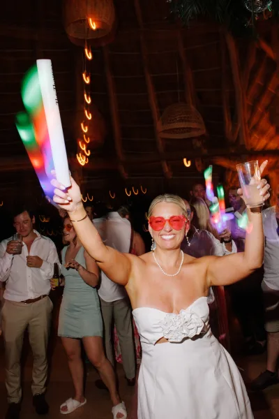 Wedding dance party with bride dancing reception in heart-shaped sunglasses and glow sticks under string lights and wicker lanterns