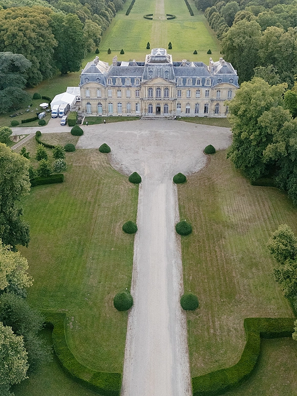 Wedding venue exterior of a chateau wedding venue with a white reception tent, service vans, and a gravel drive by manicured topiary gardens