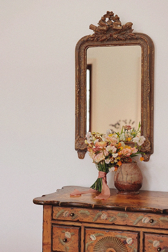 Bridal bouquet, garden style bouquet of pastel flowers with pink ribbon wrap in a ceramic vase beside an antique mirror on a wooden dresser