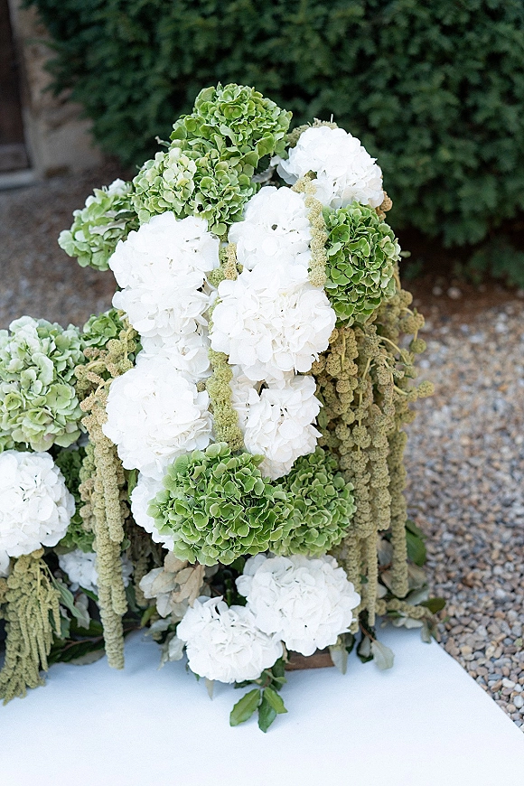 Wedding florals with hydrangea wedding flowers in white and green, cascading amaranthus and greenery beside a white aisle runner on gravel
