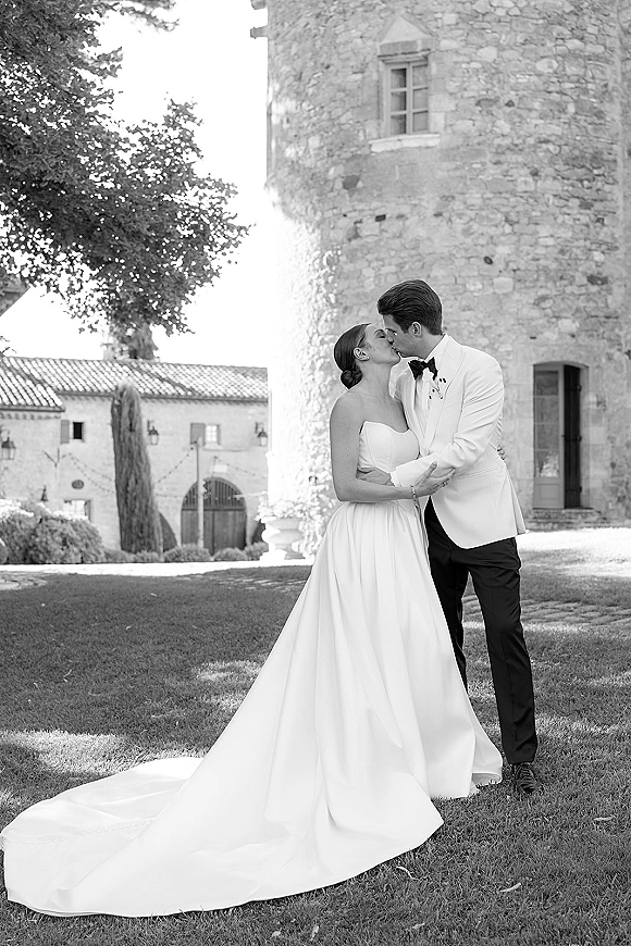 Wedding kiss portrait of bride and groom kissing in a black and white wedding photo, full-length in a courtyard by a stone tower