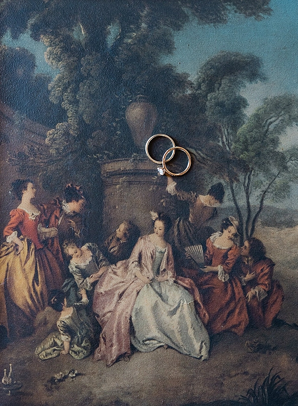 Wedding rings, gold wedding bands stacked with a diamond engagement ring on a vintage pastoral painting background flat lay