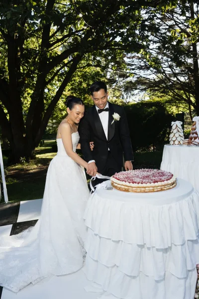 Wedding cake cutting as the bride and groom cut the cake under garden trees, beside a croquembouche tower.