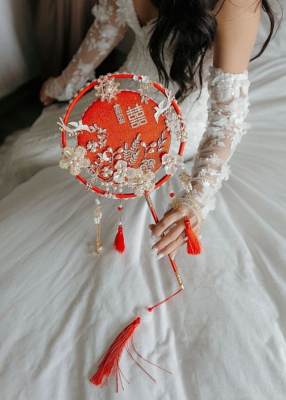 Bridal fan, red wedding fan with pearl embellishments and tassels, held by bride in lace gloves showing engagement ring in soft indoor light
