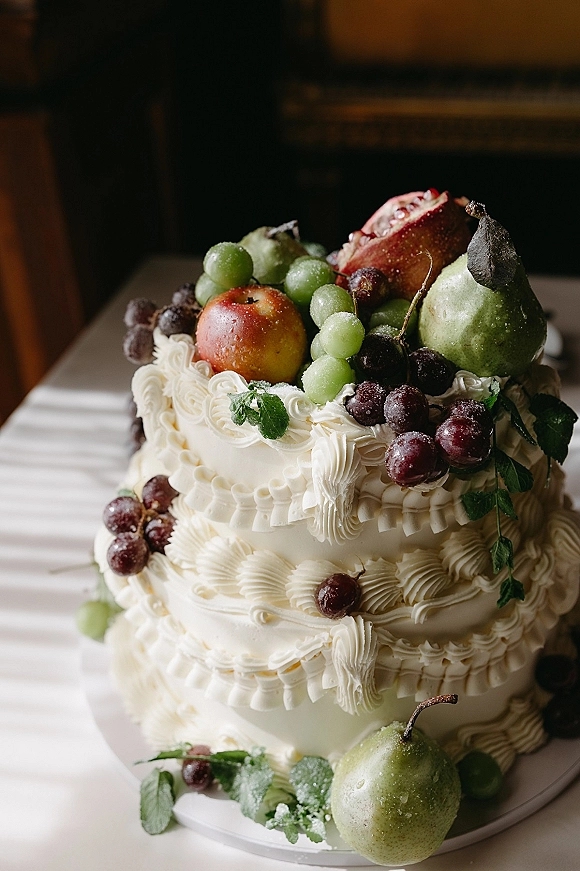 Wedding cake with fruit topped wedding cake styling, white buttercream and piped frosting, topped with grapes, pears, apple and mint on a stand