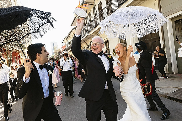 Wedding parade with bride in a wedding dress and groom in tuxedo marching under lace parasols on a city street with brass band and crowd