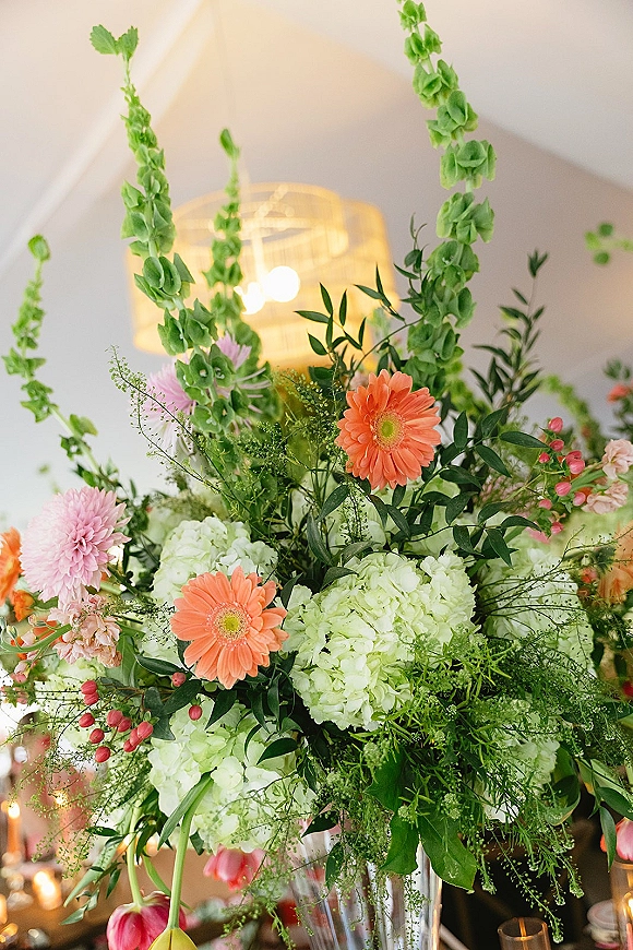 Wedding centerpiece with a tall wedding centerpiece floral arrangement of hydrangea, gerbera daisies, tulips, and greenery in a glass vase at candlelit reception