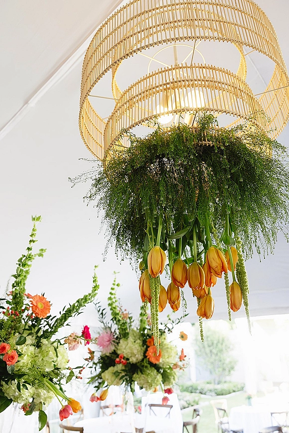 Floral chandelier with hanging greenery and tulips draped from a gold fixture beneath a white tent ceiling over reception tables