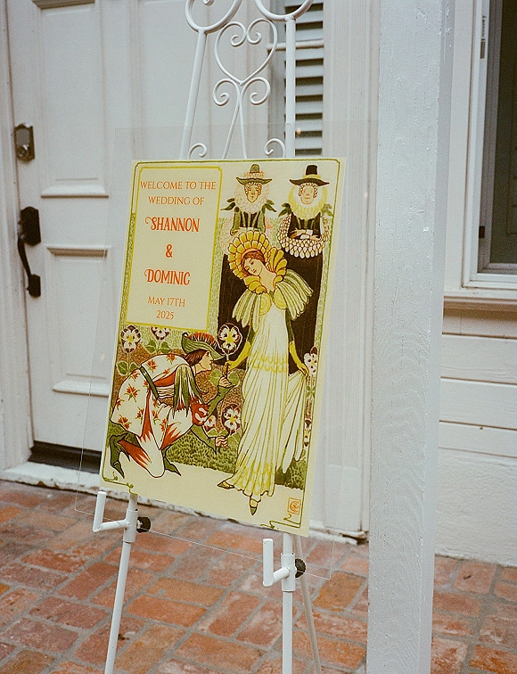 Wedding welcome sign on an easel, a custom wedding welcome sign poster set by a white exterior wall with brick walkway and shuttered window