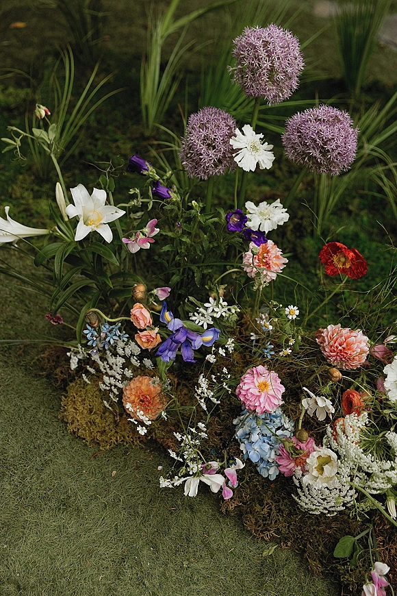 Wedding floral arrangement with ceremony ground florals featuring purple allium, hydrangea, dahlias, and moss on garden grass cover