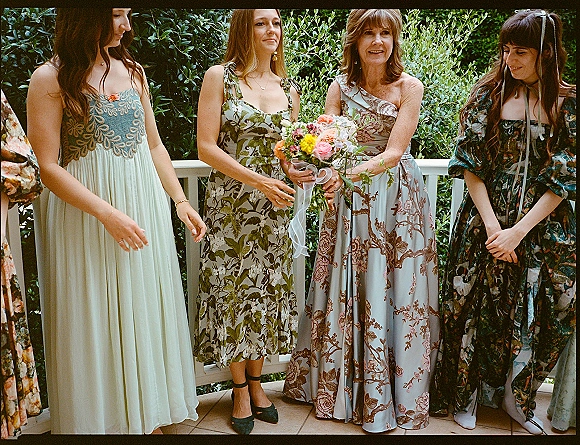 Bridesmaid group photo of bridesmaids holding bouquet, wearing mismatched floral dresses and heels on an outdoor garden patio by white railing