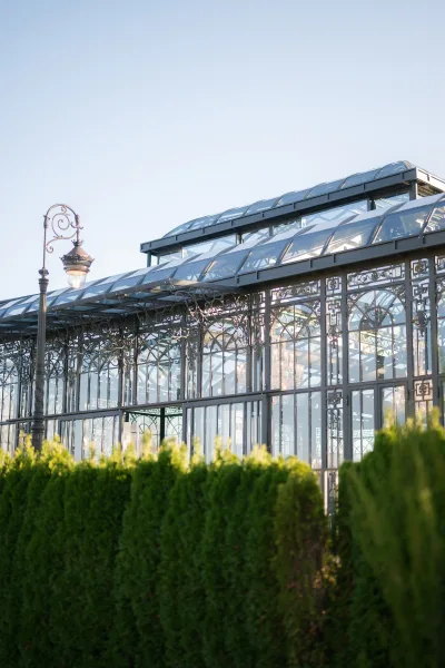 Wedding venue exterior with a glass conservatory wedding venue, wrought iron framework and street lamp, framed by green hedges under a clear sky