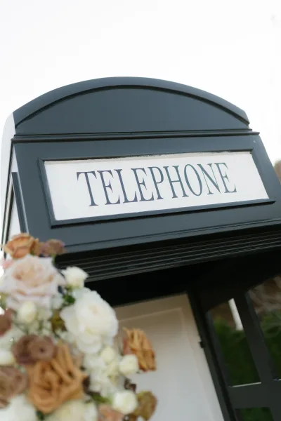 Wedding phone booth audio guest book decorated with rose florals, set outdoors against lush greenery and open sky