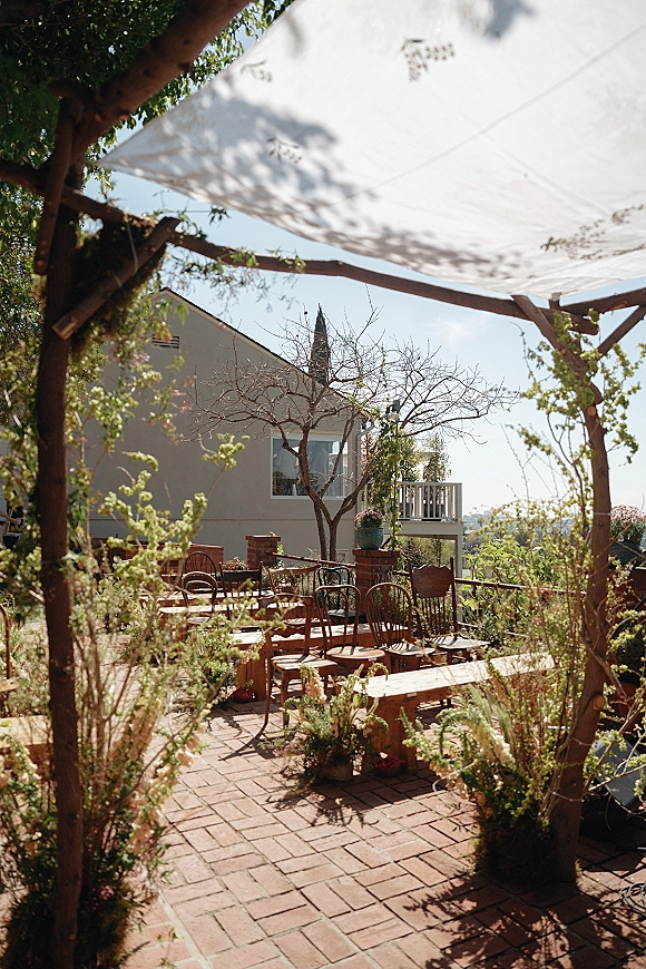 Ceremony setup with backyard wedding ceremony seating under a wood pergola and white fabric canopy on brick pavers beside a house