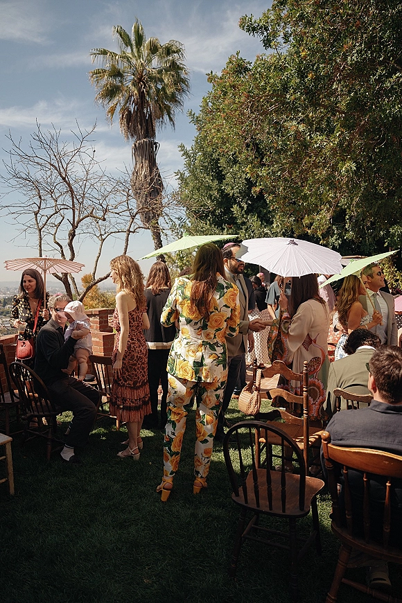 Wedding cocktail hour with outdoor wedding cocktail hour guests mingling on a sunny lawn, some under parasol umbrellas by palm trees