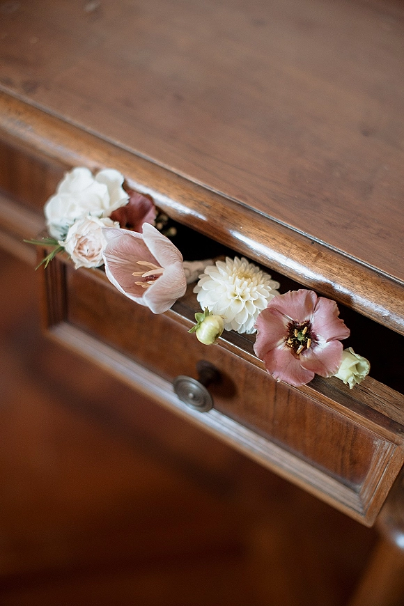Wedding floral detail with blush tulip and white dahlia stems tucked in an open wooden dresser drawer, ivory rose and greenery nearby