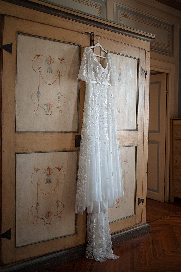 Wedding dress with lace wedding dress details hanging on a hanger, featuring a V-neck and tulle skirt against a vintage armoire backdrop
